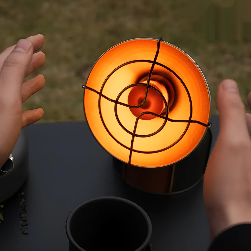 Black and orange mini portable camping stove with automatic ignition on a grassy outdoor surface.