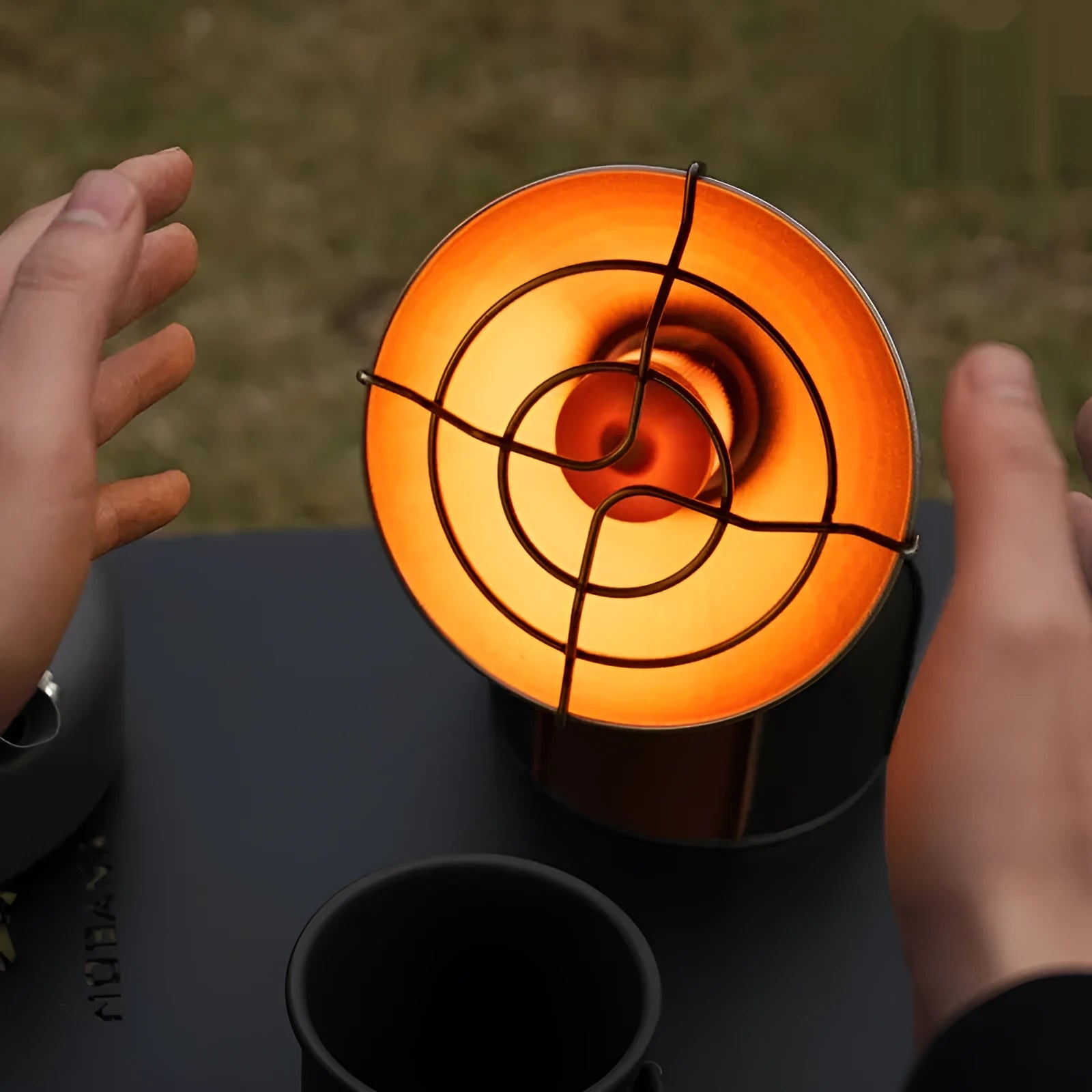 Black and orange mini portable camping stove with automatic ignition on a grassy outdoor surface.