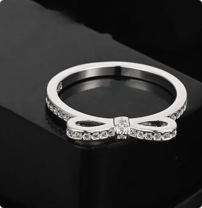 Close-up of a silver-tone bow-shaped ring with sparkling zircon crystal accents on a hand.
