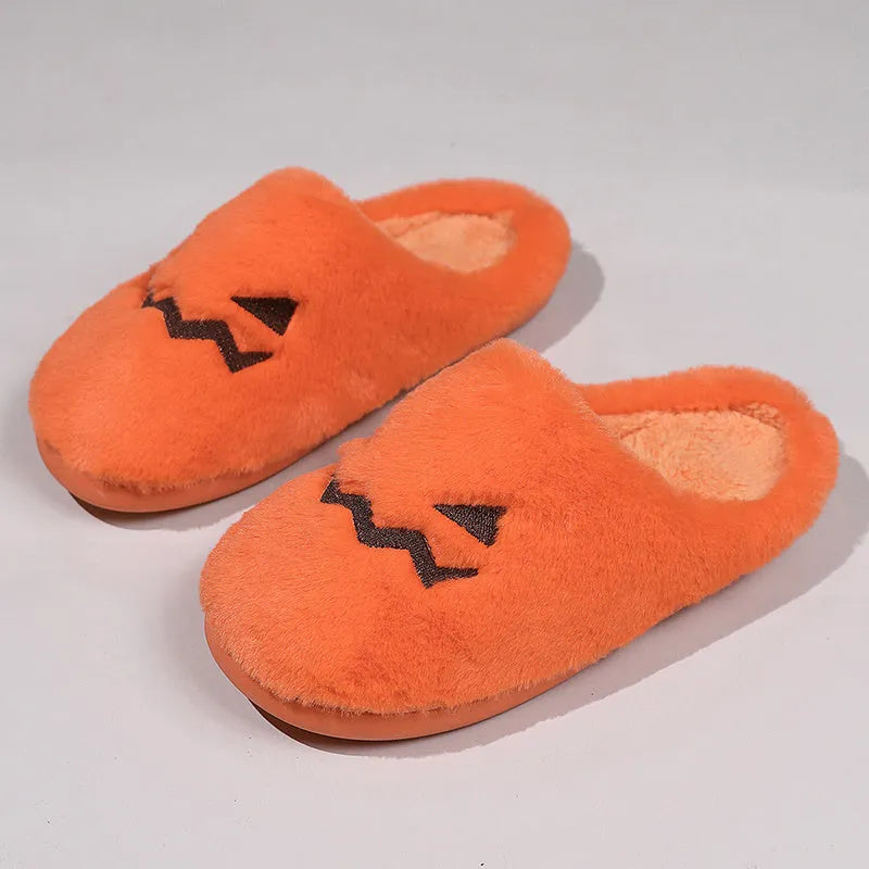 Orange Halloween pumpkin-themed plush indoor slippers with a non-slip sole on a wooden floor.