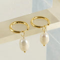 A pair of gold-colour geometric drop earrings with white pearl accents on a stainless steel post.