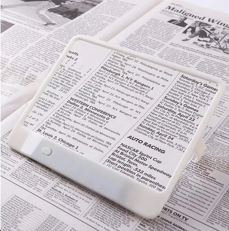 Black or white magnifying glass with integrated LED reading lamp, showing 180x140mm size and 3x magnification lens.