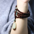 Close-up of a hand-carved rosewood beaded bracelet with 108 6mm beads and a carved Hotian jade pendant.