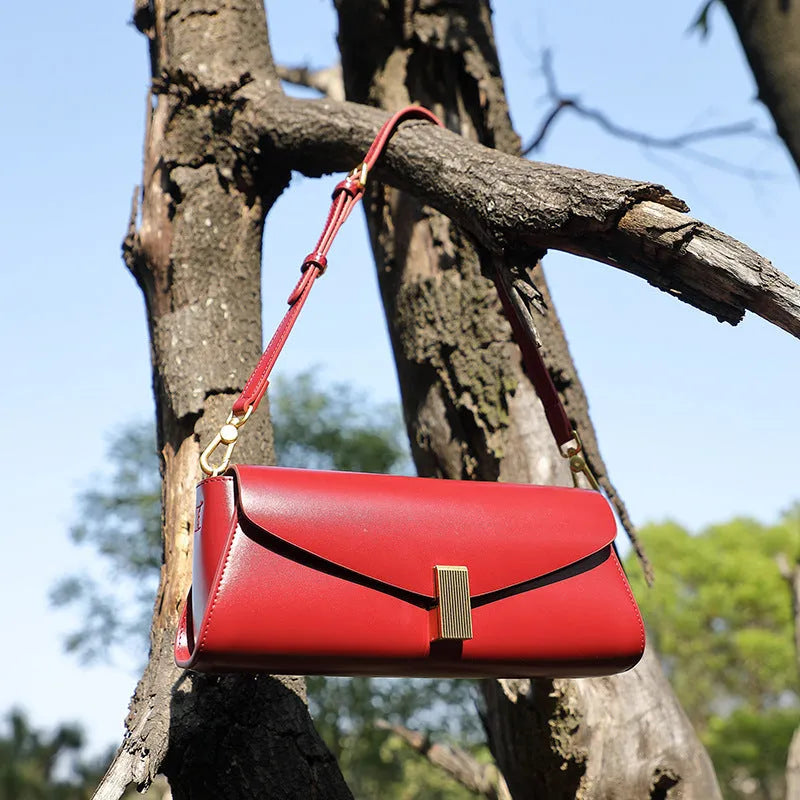 Cowhide leather cross-body shoulder bag in pillow shape with clamshell opening showing internal phone and document pockets