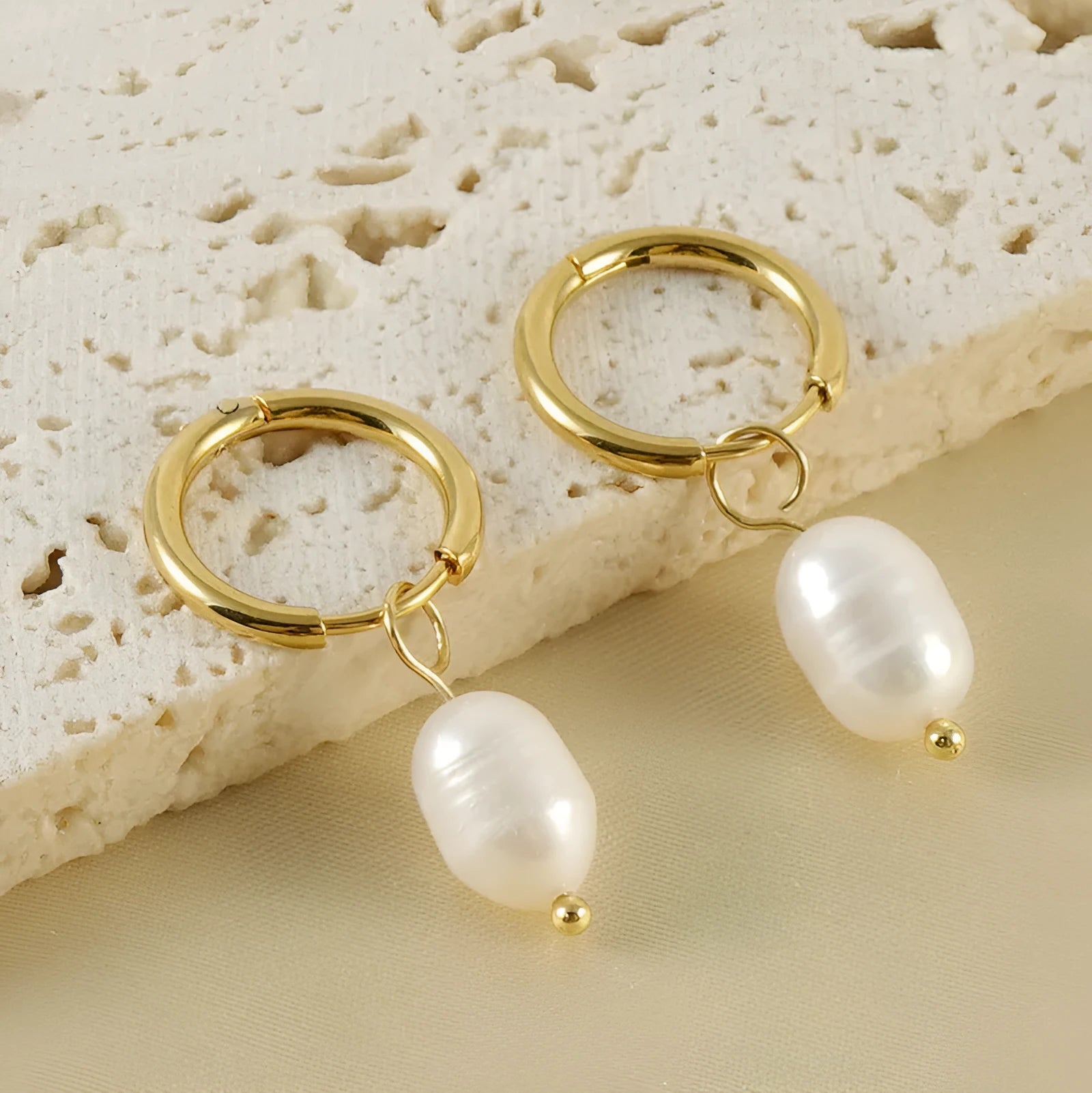 A pair of gold-colour geometric drop earrings with white pearl accents on a stainless steel post.
