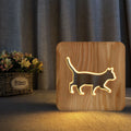 Square solid wood night light with hollow 3D cat silhouette, shown lit with warm glow.
