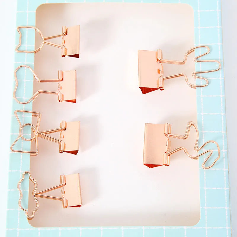 Gold metal alloy paper clip with decorative bow shape top on white background.