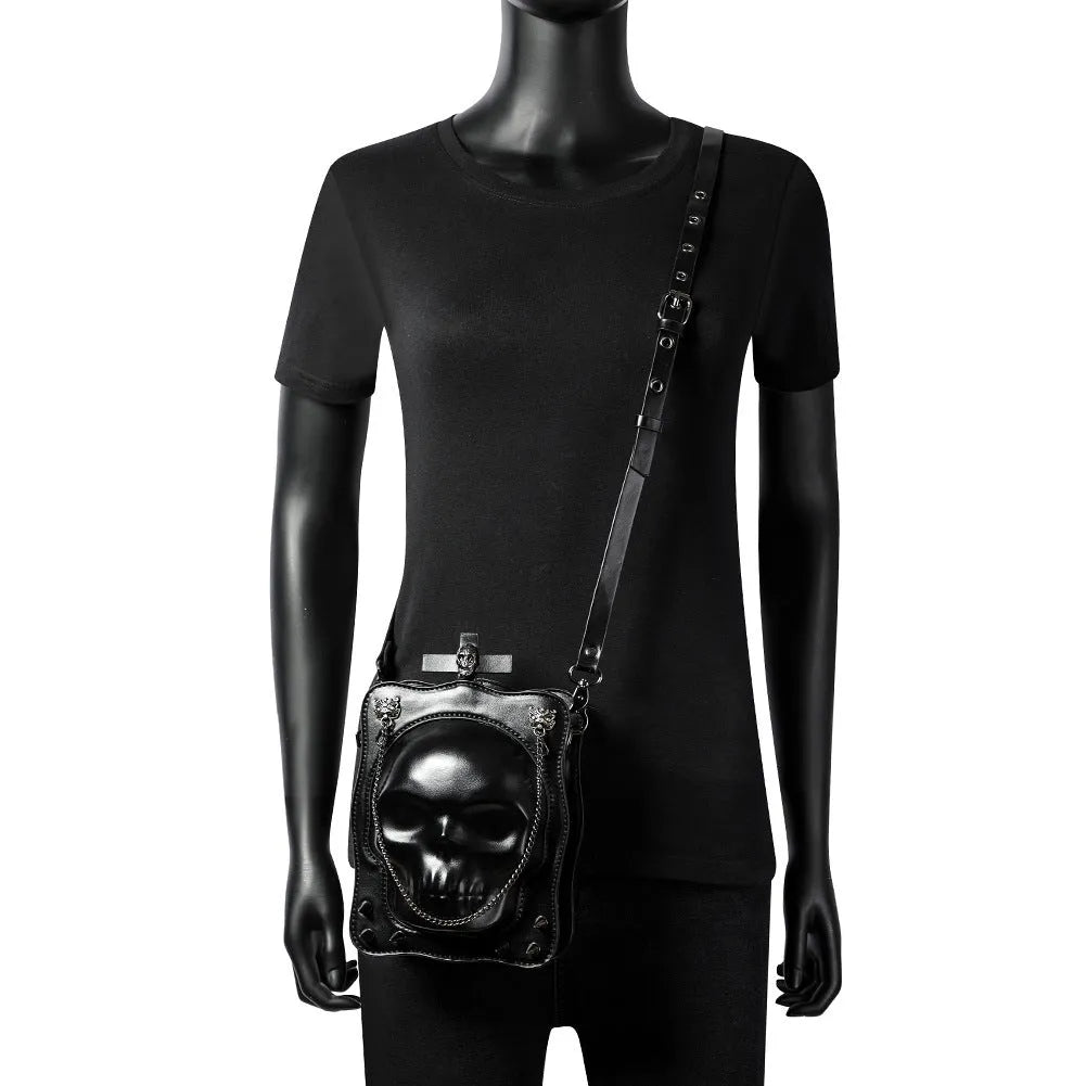 Black vertical square mini crossbody bag with embossed skull design, metal chain strap, and zipper closure