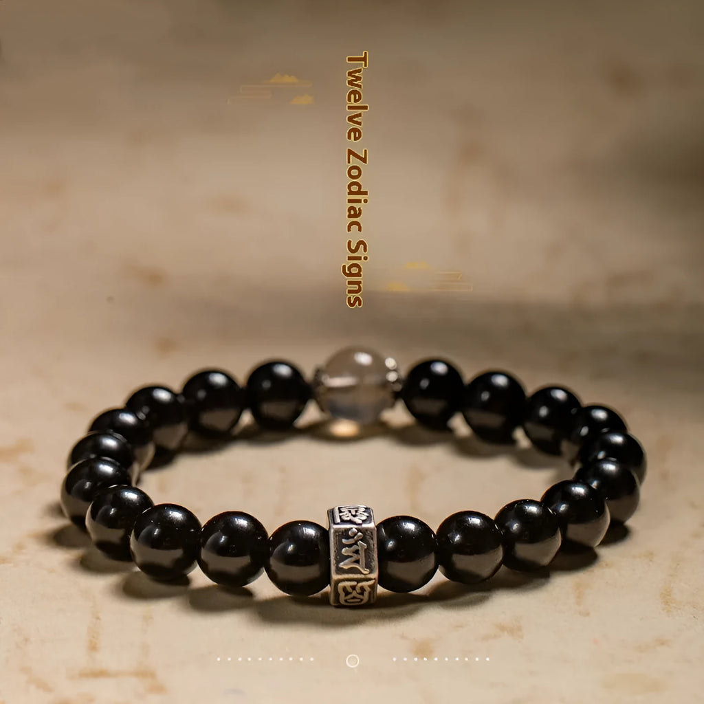 Obsidian bead bracelet with a hand-carved zodiac animal and bodhisattva charm on a wrist.