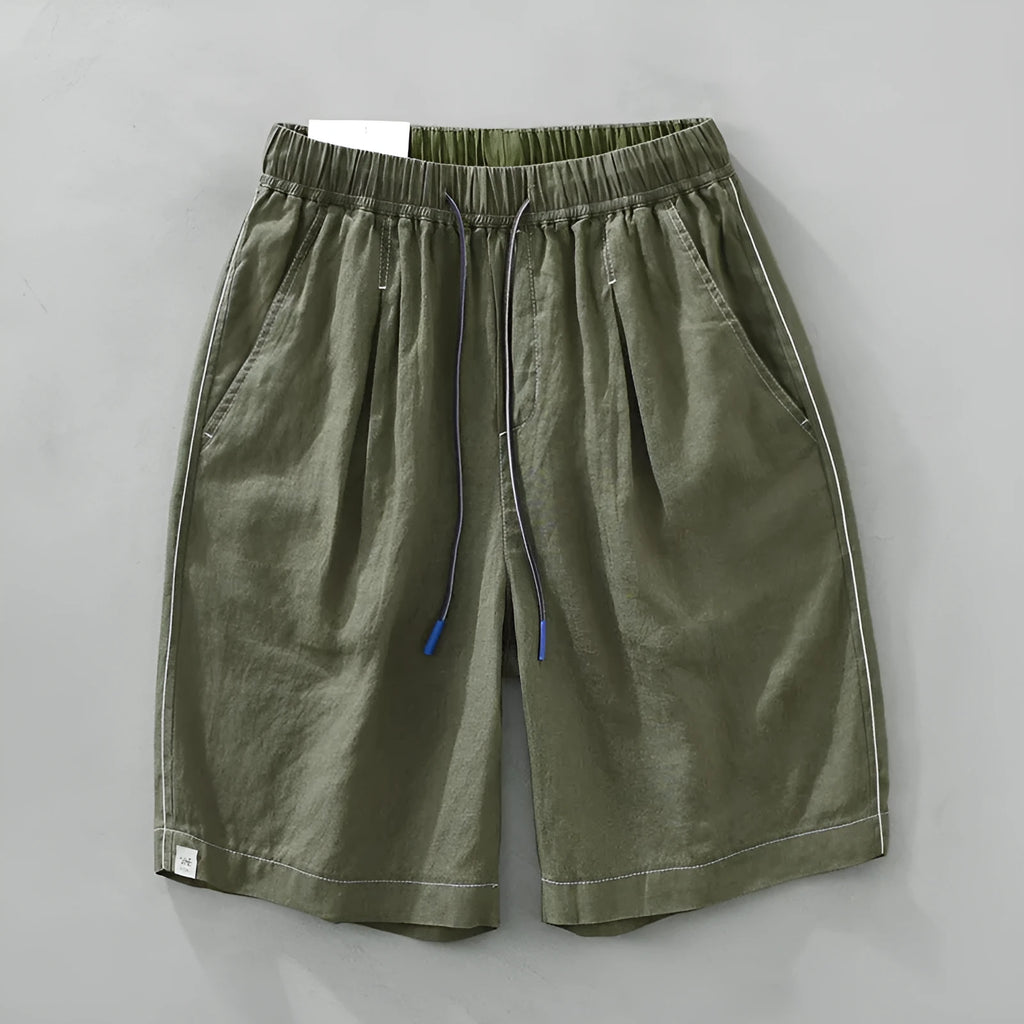 Man wearing loose fit green linen shorts with a straight leg and drawstring waist for casual summer wear.