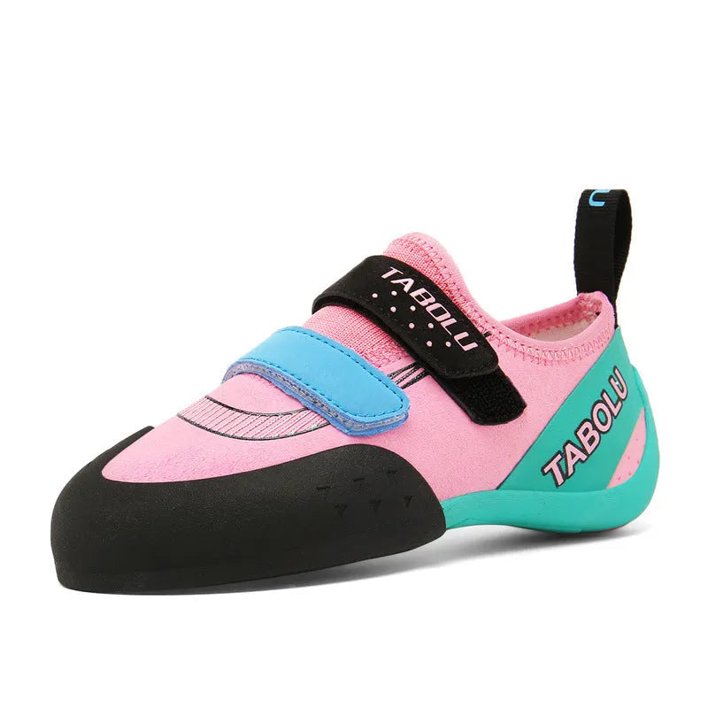 A pair of beginner rock climbing shoes with Velcro straps and a coloured trim, shown on a rocky surface.