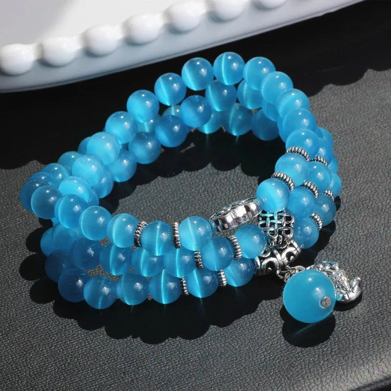 Women's opal bracelet with lucky cat charm, shown in a triple-wrap style with colourful geometric beads.