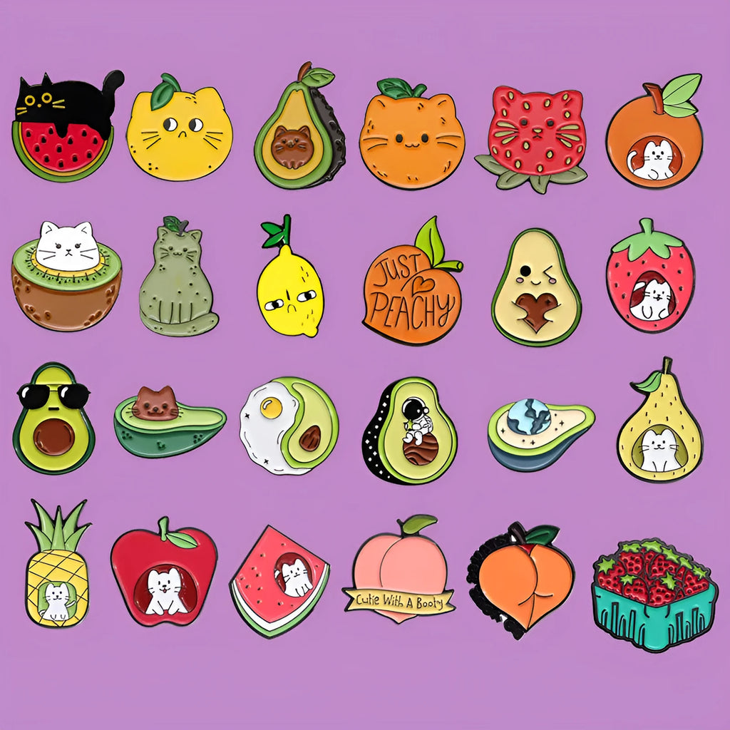 Close-up of a colourful cartoon-style fruit and letter metal brooch with a pin back on a fabric background.