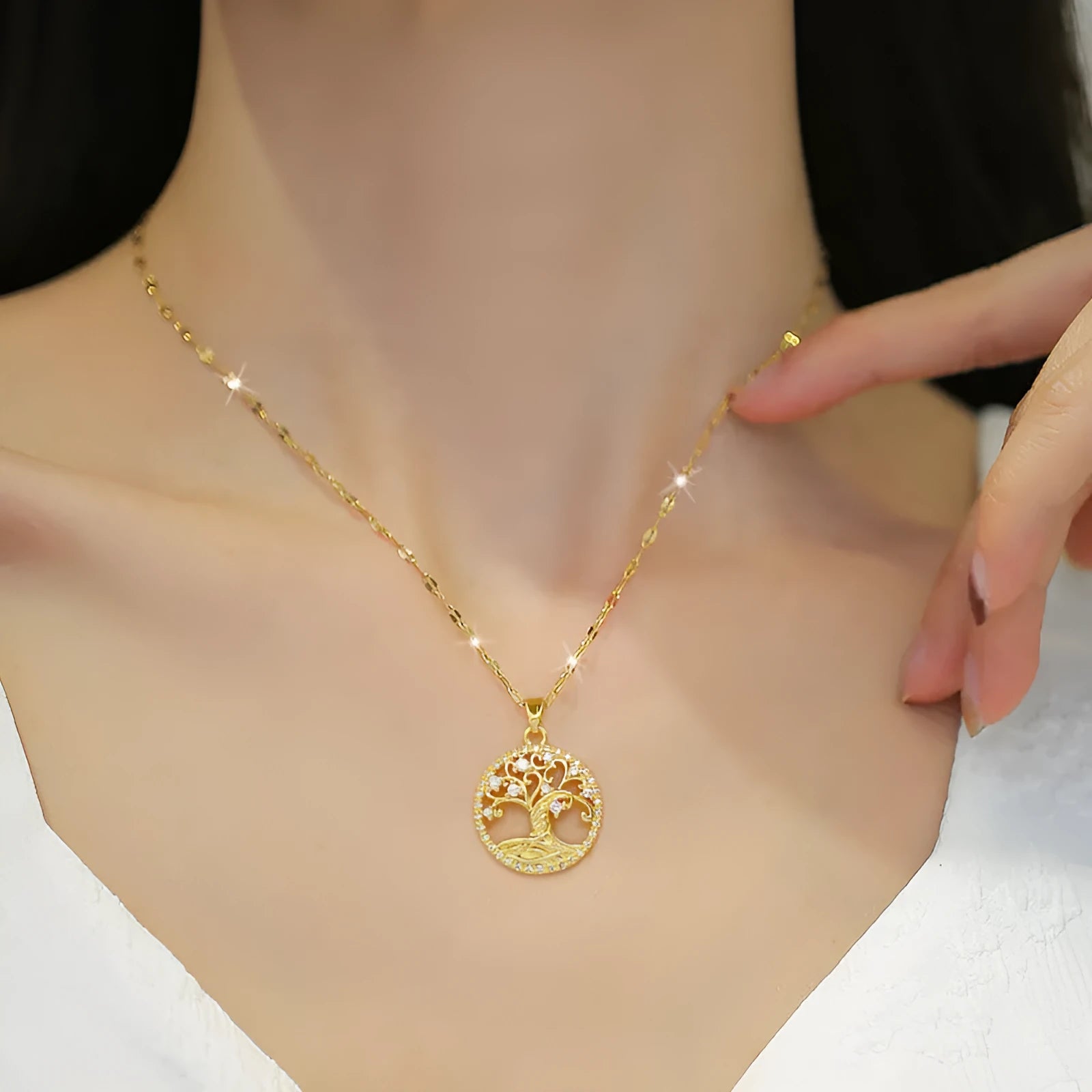 Close-up of a gold necklace with an ornate tree pendant featuring sparkling crystals and a white mother-of-pearl centre, on an adjustable chain.