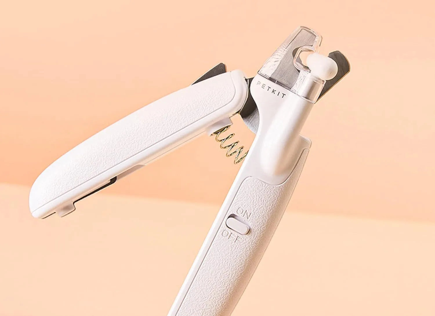 White pet nail clippers with LED light and transparent guard, shown with a separate nail file on a table.