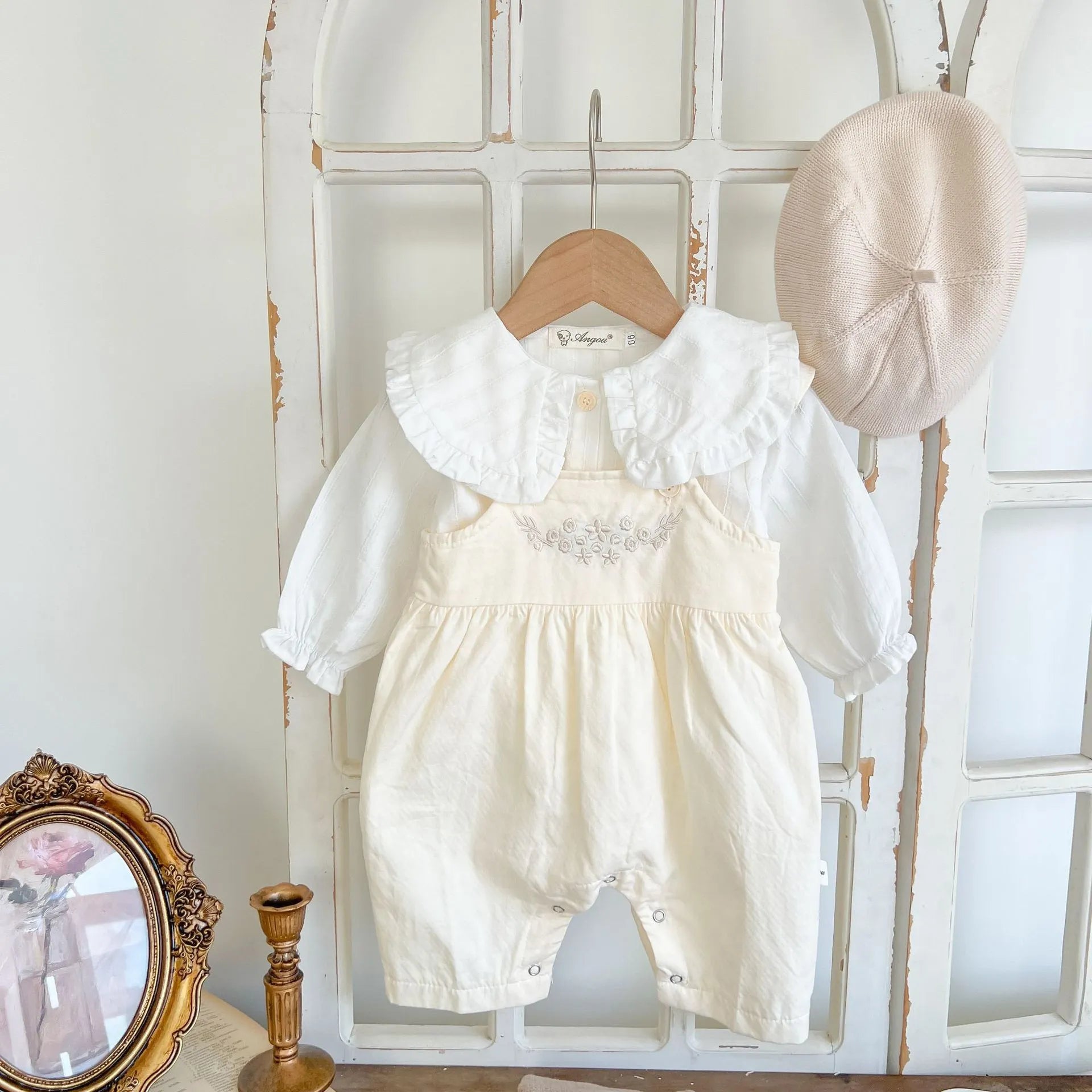 Baby girl wearing a loose-fit cotton suspender romper with adjustable straps in an apricot colour.