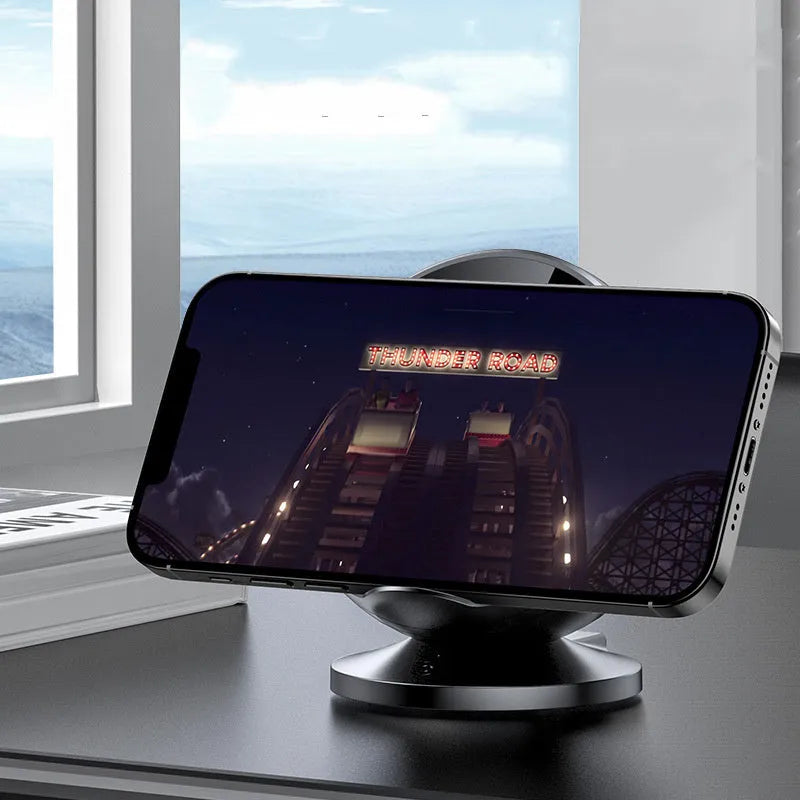 A black multifunctional mobile phone holder with integrated wireless charger and Bluetooth speaker on a desk.