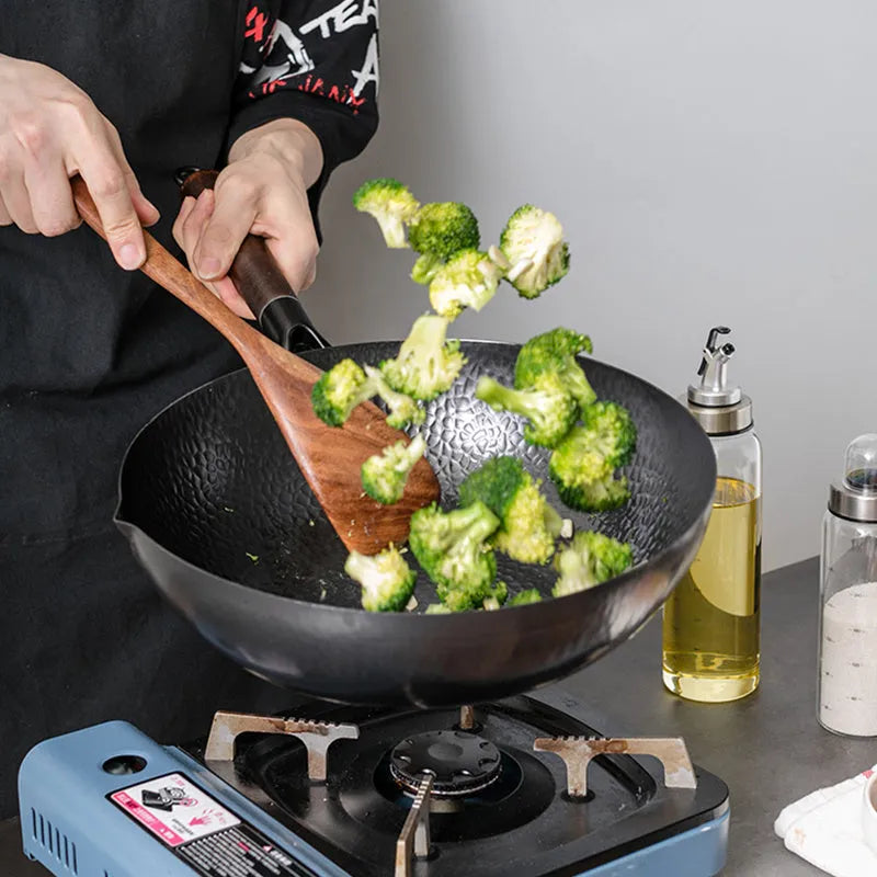 Traditional black iron wok with a long wooden handle on a kitchen counter.