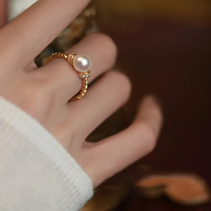 Close-up of an adjustable geometric twist ring in copper with a central pearl inlay, shown on a finger.