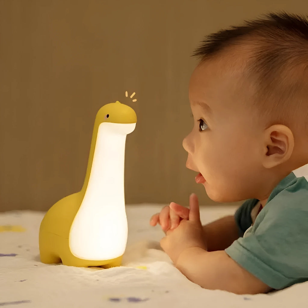Dinosaur night light in lemon yellow with warm 3000K glow on a bedside table, USB charging cable included