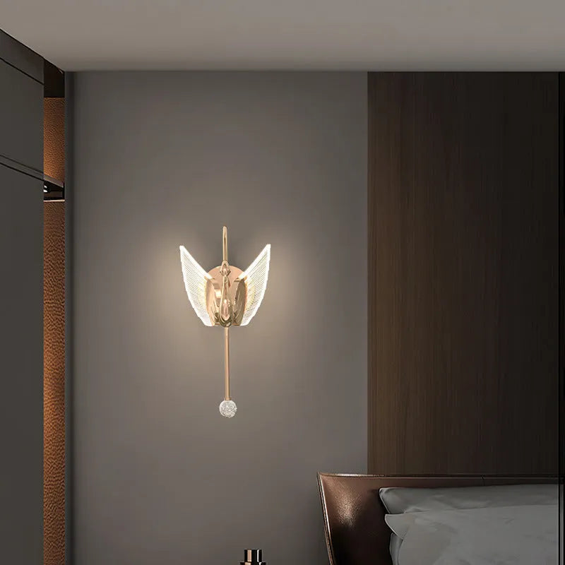 Gold modern swan-shaped wall lamp with acrylic shade mounted beside a bed.