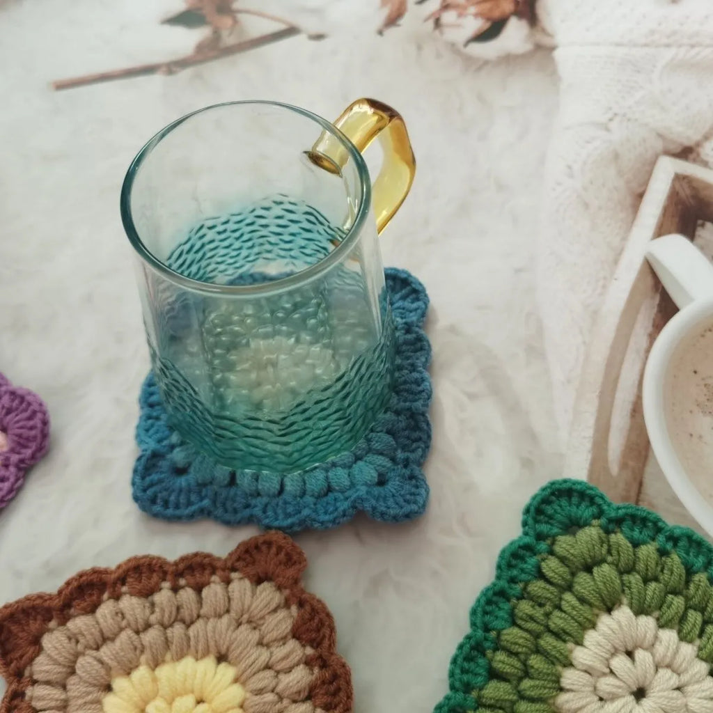 Hand-crocheted wool coaster with lattice pattern in Dream Purple colour on a wooden table.