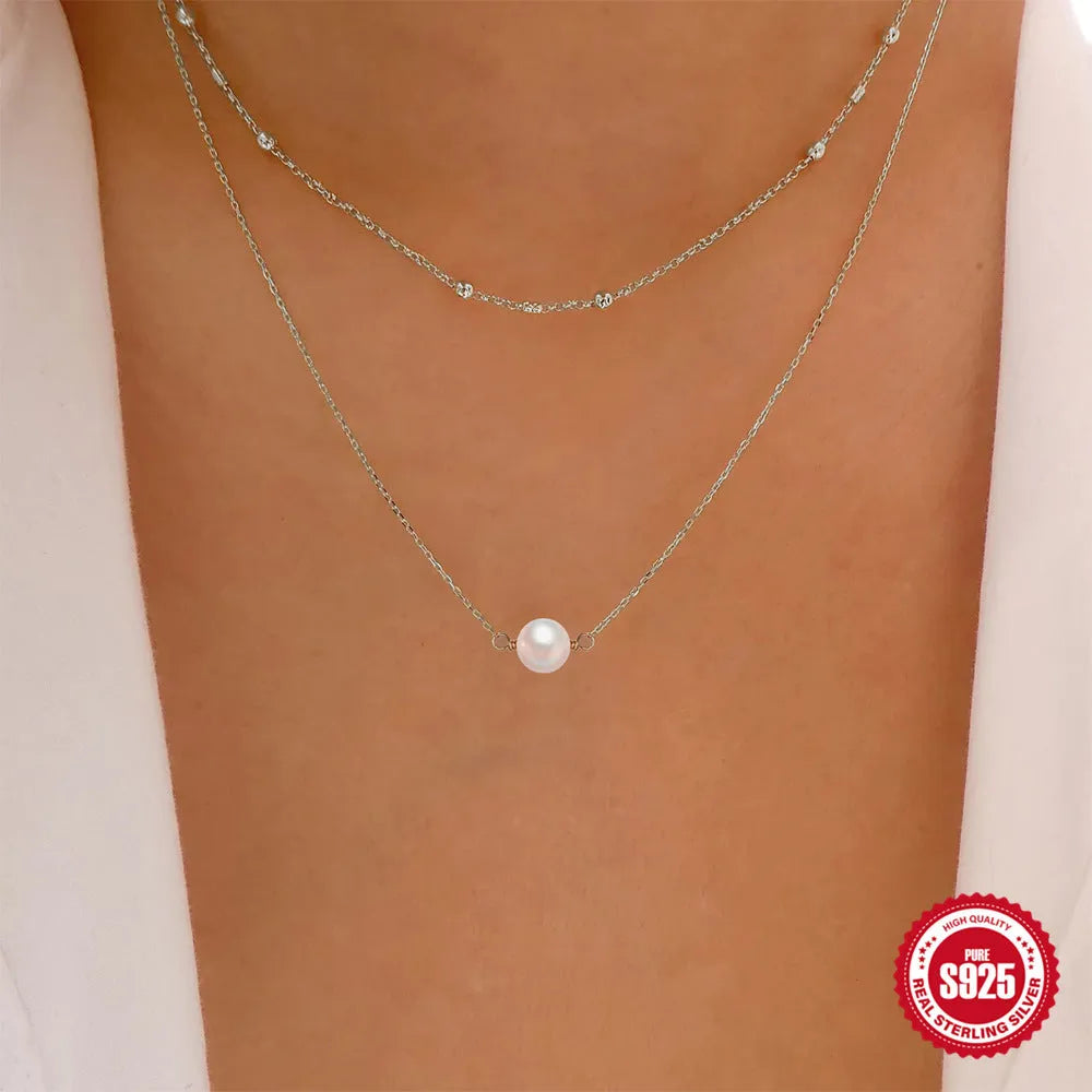 Close-up of a double-layer sterling silver necklace with twin pearl geometric pendants on a ball bead chain.