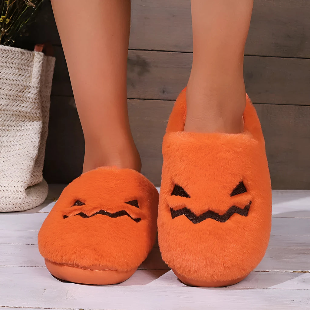Orange Halloween pumpkin-themed plush indoor slippers with a non-slip sole on a wooden floor.