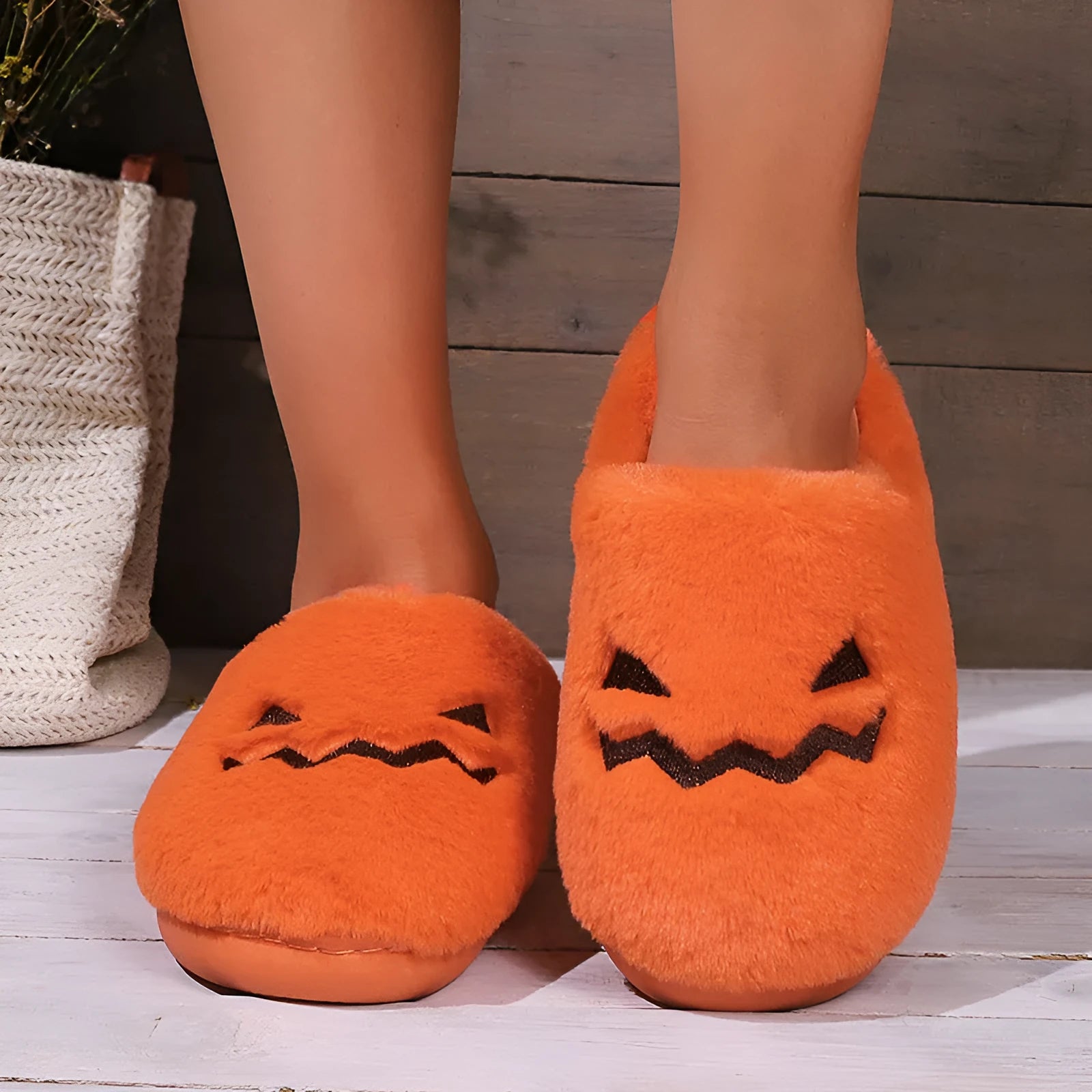 Orange Halloween pumpkin-themed plush indoor slippers with a non-slip sole on a wooden floor.