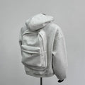 Man wearing a light gray hooded coat with a schoolbag design detail on the back.
