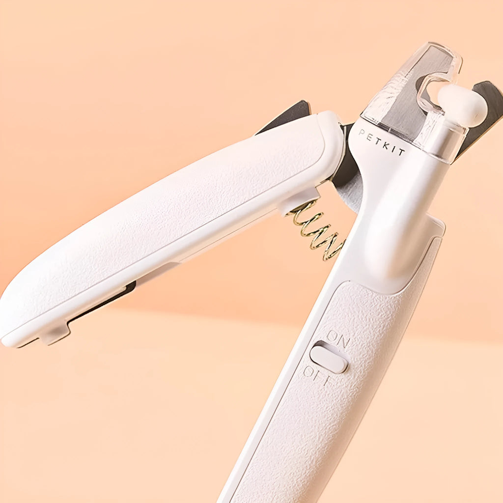 White pet nail clippers with LED light and transparent guard, shown with a separate nail file on a table.