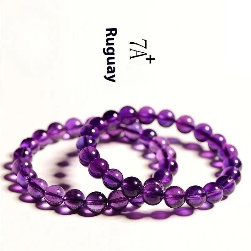 Close-up of a polished natural amethyst bead stretch bracelet on a wrist, showing deep violet colour and elasticated band.