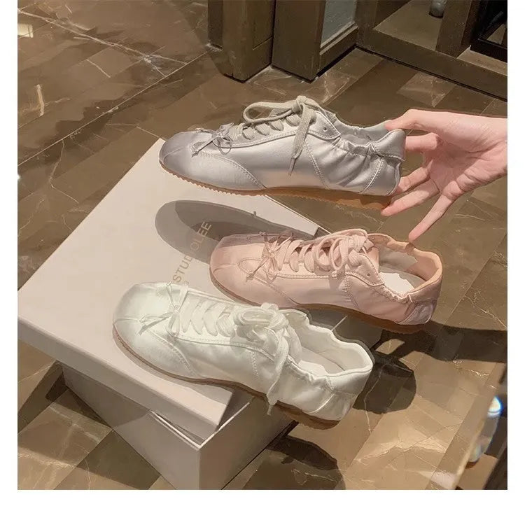 Women's champagne pink satin ballet flats with front lace-up and round toe on a white background.