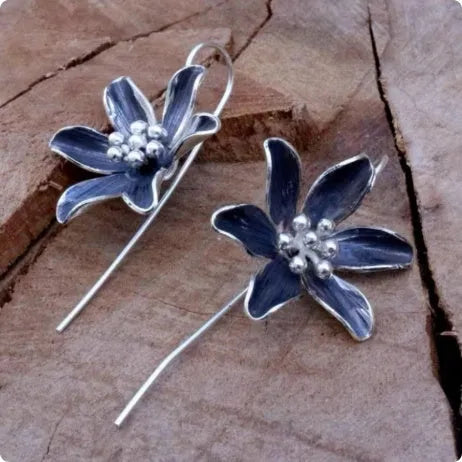 A pair of purple flower-shaped alloy earrings with an electroplated finish on a white background.
