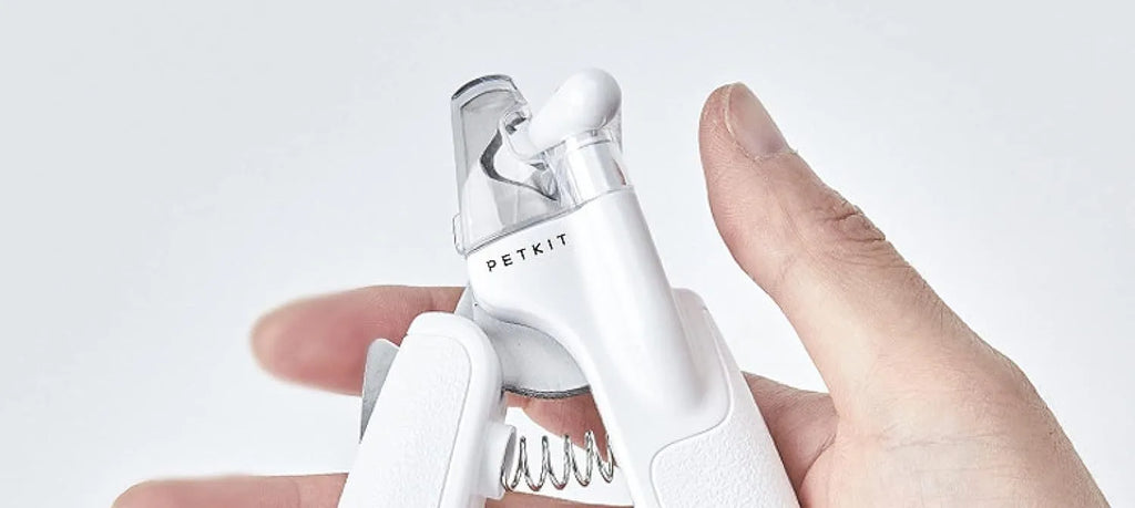 White pet nail clippers with LED light and transparent guard, shown with a separate nail file on a table.