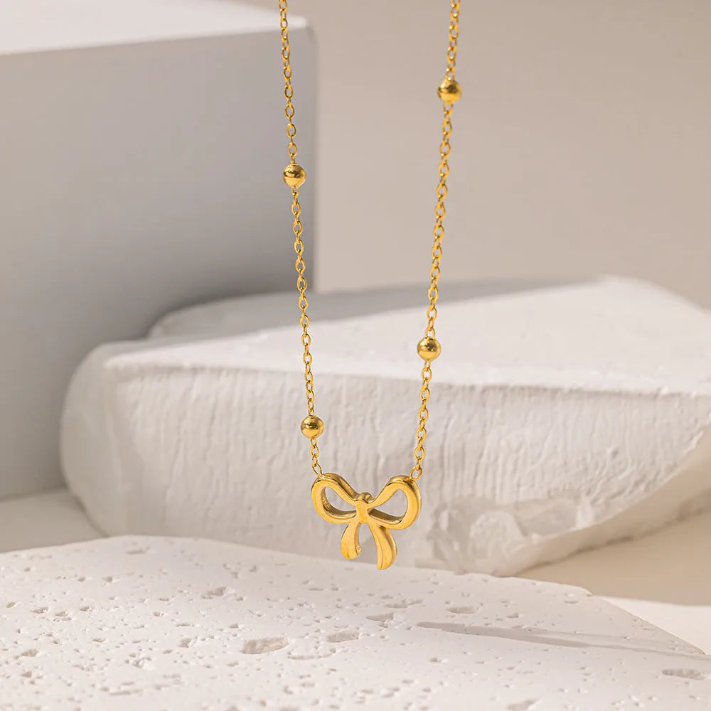Gold electroplated titanium steel bow necklace with cross chain design showing adjustable length mechanism