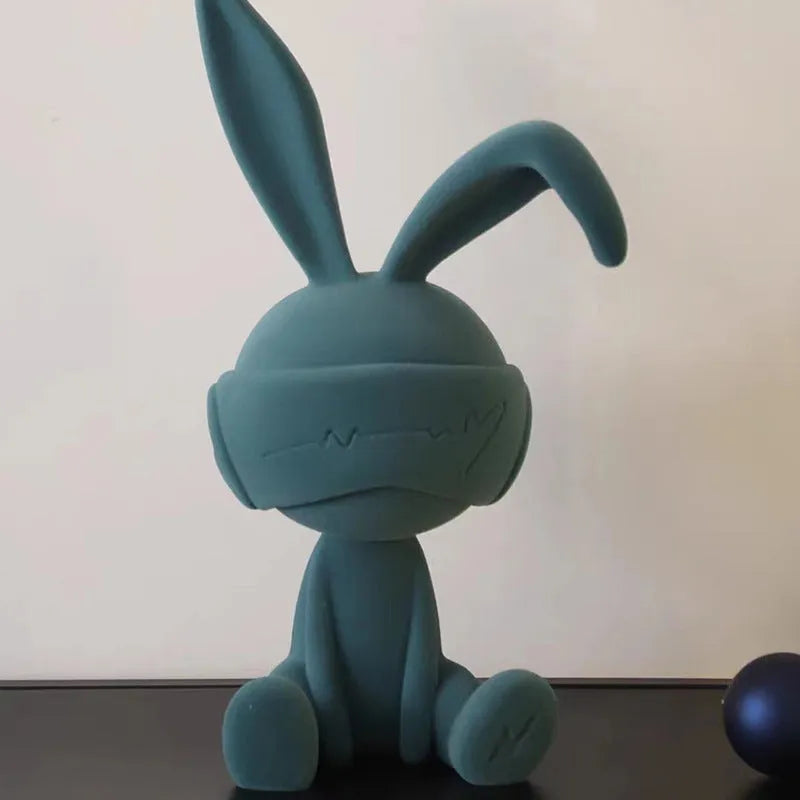 Suede blindfold rabbit resin ornament in blue, green, or red colour on a table.