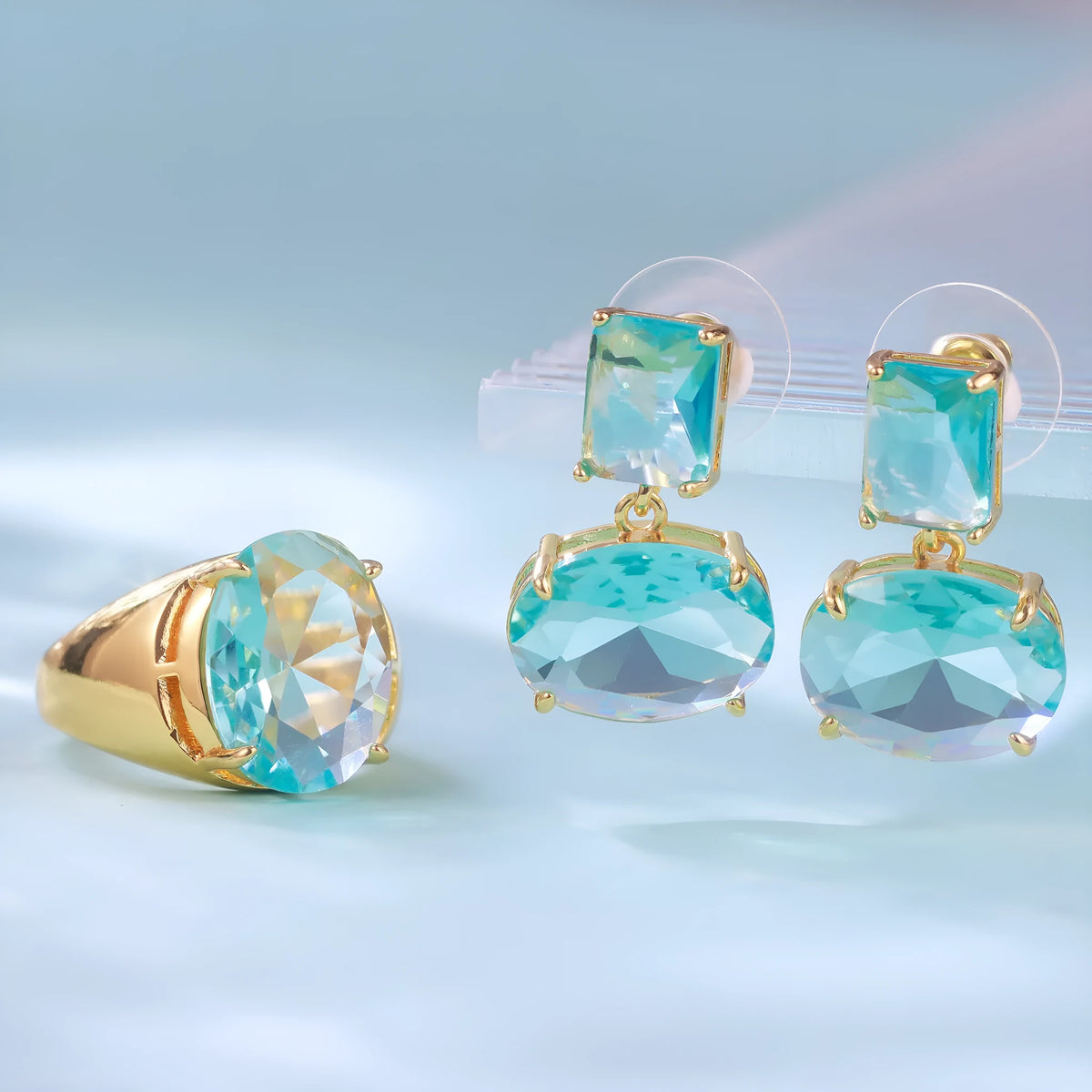 Pair of geometric earrings with gold plated copper base and golden blue glass pendant in ellipse shape on white background