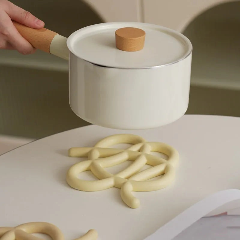 Irregular-shaped ceramic heat proof mat in grey on a wooden table next to a hot pan.