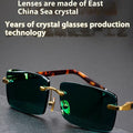 Frameless sunglasses with dark green tinted lenses and a black hard-shell case on a table.