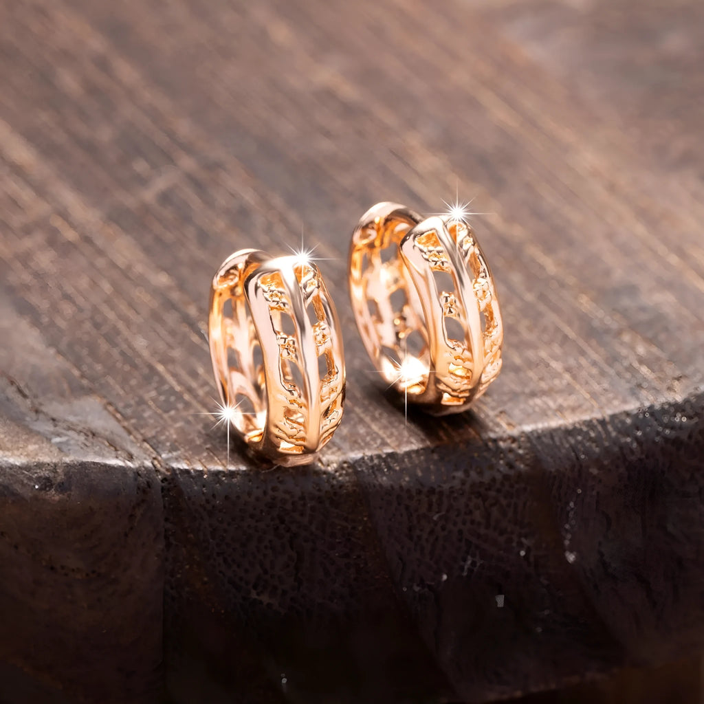 Close-up of rose gold plated copper stud earrings with hollow leaf and heart shapes on a grey background.