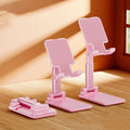 White folding telescopic mobile phone holder with silicone pad on a desktop, holding a smartphone at an angle.