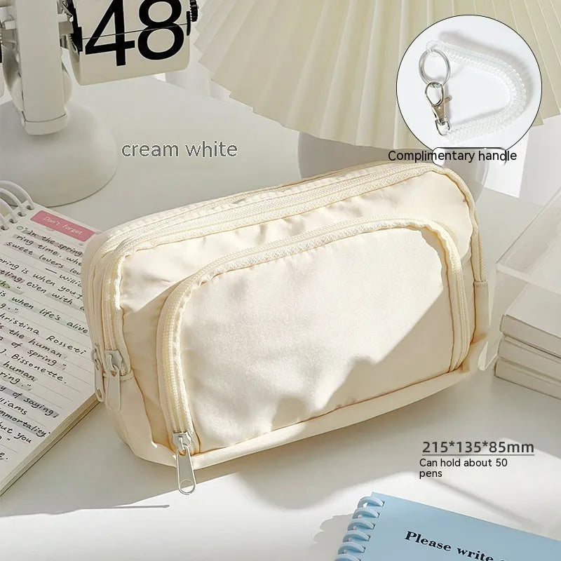 Double layer pencil case in pink with a gift handle, shown next to pens and pencils.