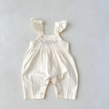 Baby girl wearing a loose-fit cotton suspender romper with adjustable straps in an apricot colour.
