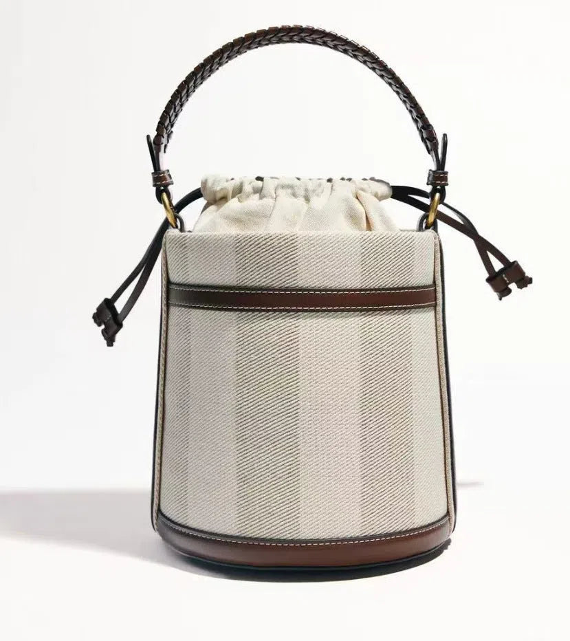 Brown PU cylindrical tote bag with dual handles, cross-body strap, and woven stitch detailing on a white background