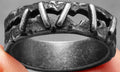 Close-up of a stainless steel double ring with dark punk stitching-style texture on the band.