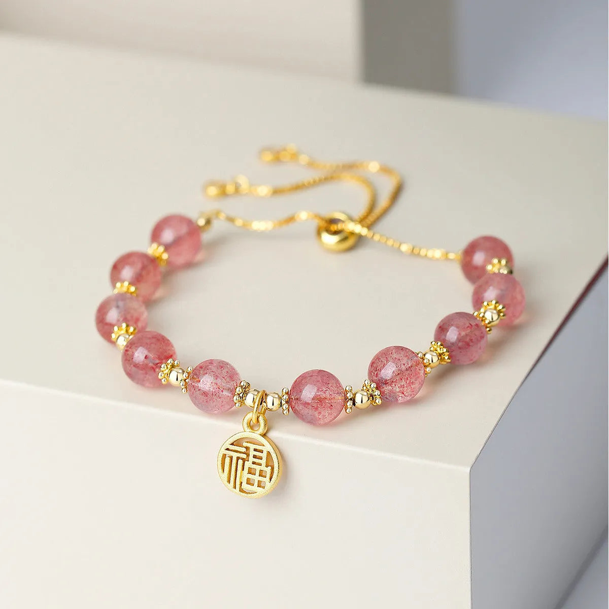 Women's strawberry quartz bracelet with a geometric fu character charm on an electroplated chain.