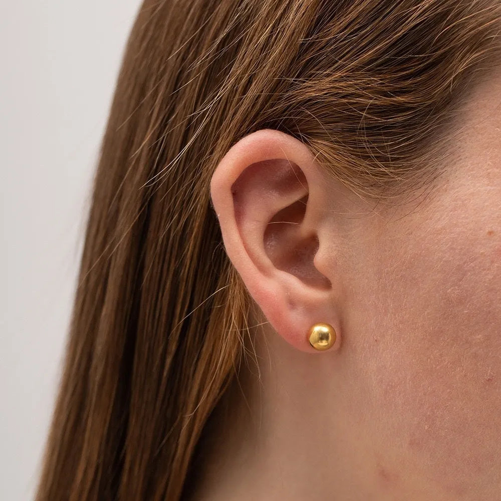 Close-up of a small spherical stainless steel stud earring with a polished electroplated finish on a grey background.