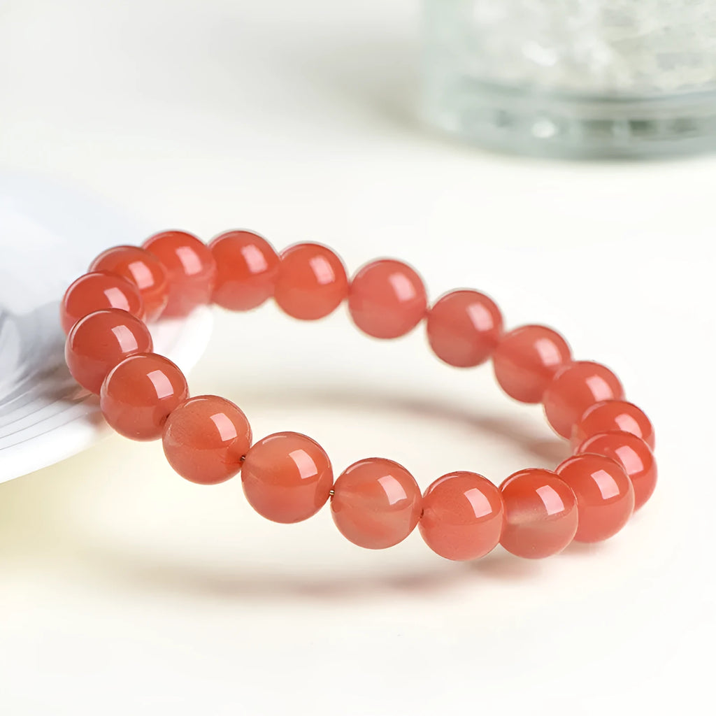 Natural cherry red agate beaded bracelet with adjustable metal clasp on a wrist, showing scattered polished stones.