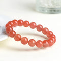 Natural cherry red agate beaded bracelet with adjustable metal clasp on a wrist, showing scattered polished stones.